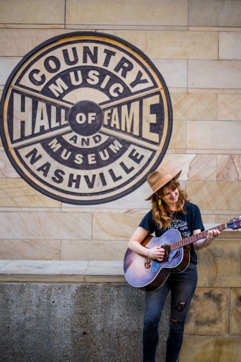 Woman with guitar standing in front of Hall of Fame and Museum in Nashville 
