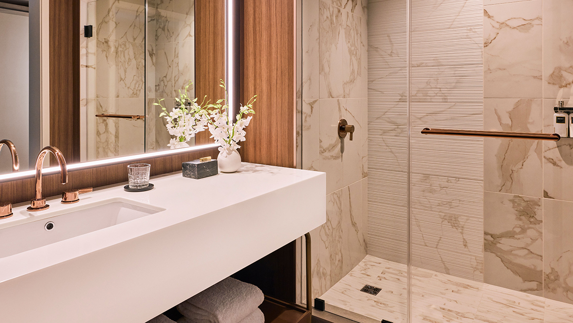 The Patron Tower bathroom with a walk-in shower is cladded in textured and smooth wall tile and warm metal finishes - Omni Boston Hotel at the Seaport